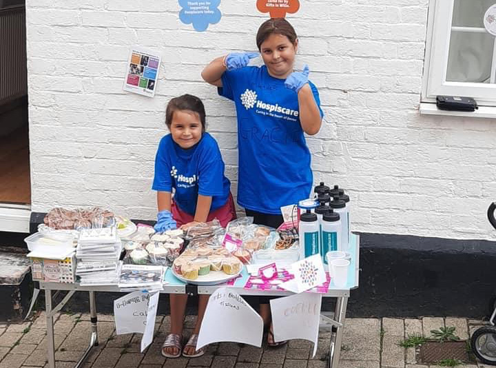 Two girls wearing Hospiscare t-shirts behind a lemonade stand