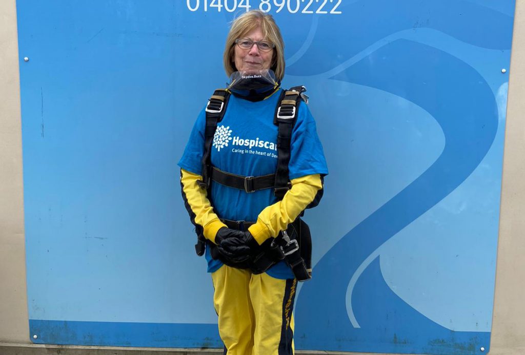 A woman in front of a blue background wearing skydiving gear