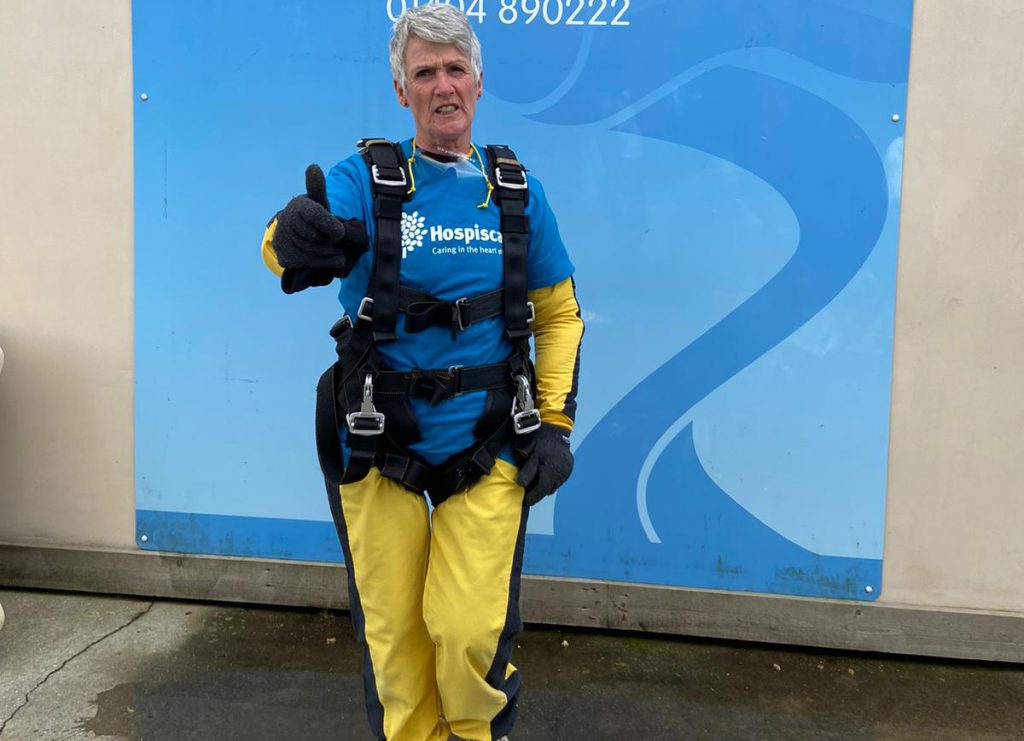 A woman wearing skydiving gear pointing at the camera