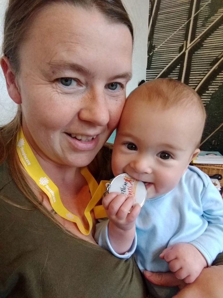 A baby chewing a medal held by a woman