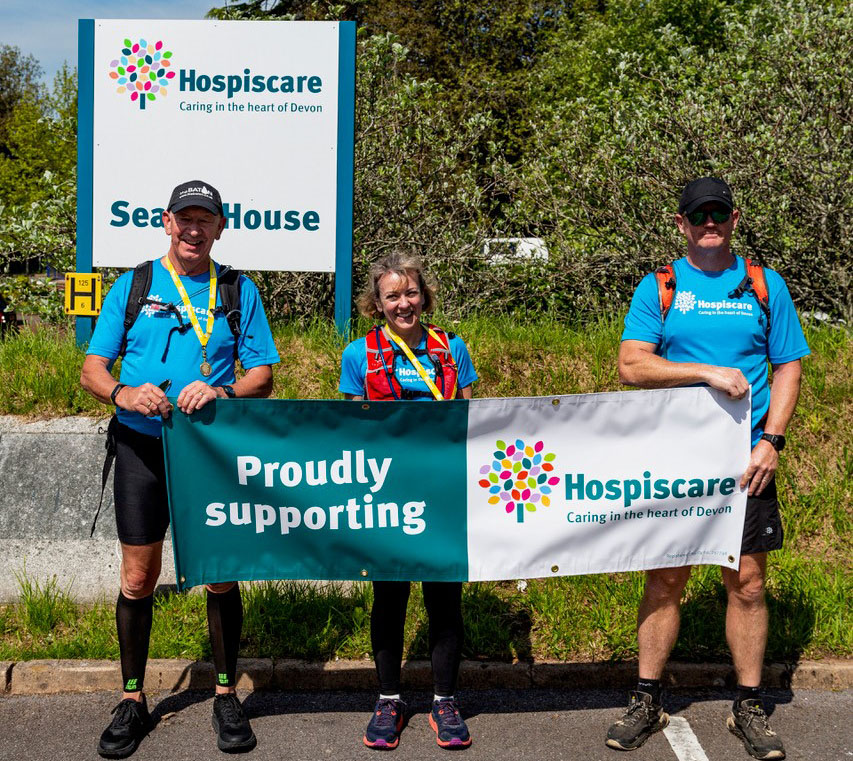 Two men and a woman holding a Hospiscare banner outside