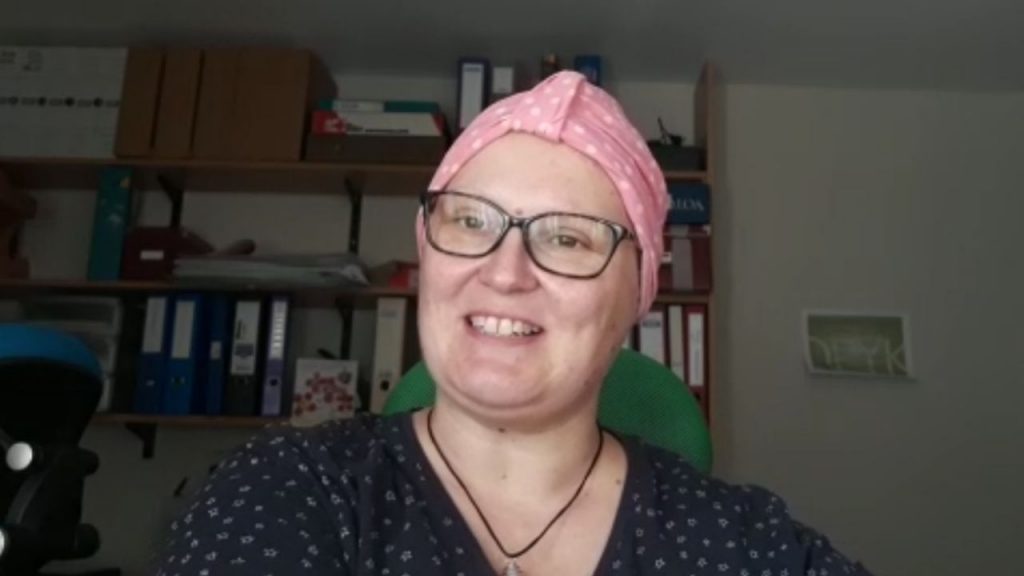 A woman wearing a pink headscarf and glasses smiling