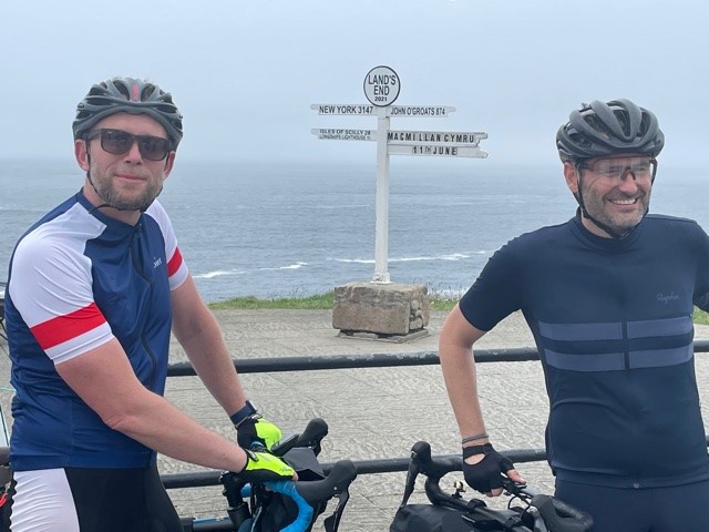 Two men in cycling gear by a coastal path sign