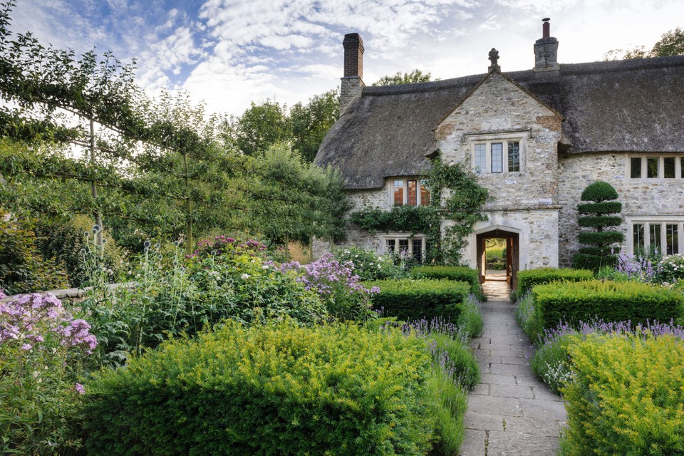 A thatched cottage with hedgerows and garden in the foreground
