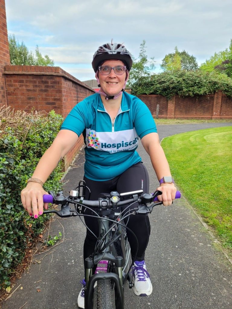 A woman wearing a Hospiscare top sitting astride a cycle