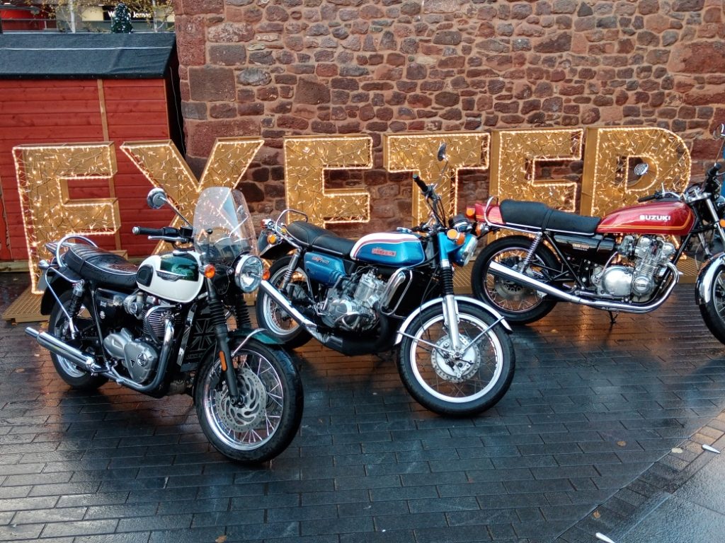 Classic motorbikes parked in front of an Exeter sign made of lights