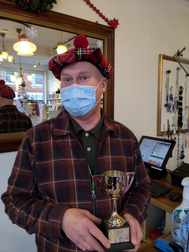 A man wearing a tartan mask and holding a trophy