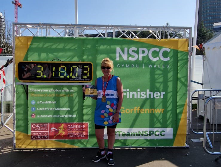 A woman standing in front of a digital time clock and NSPCC banner