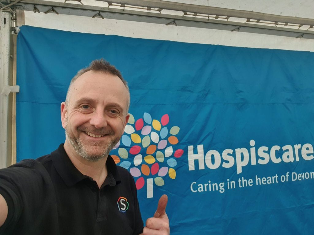 A man in front of a Hospiscare banner giving a thumb's up