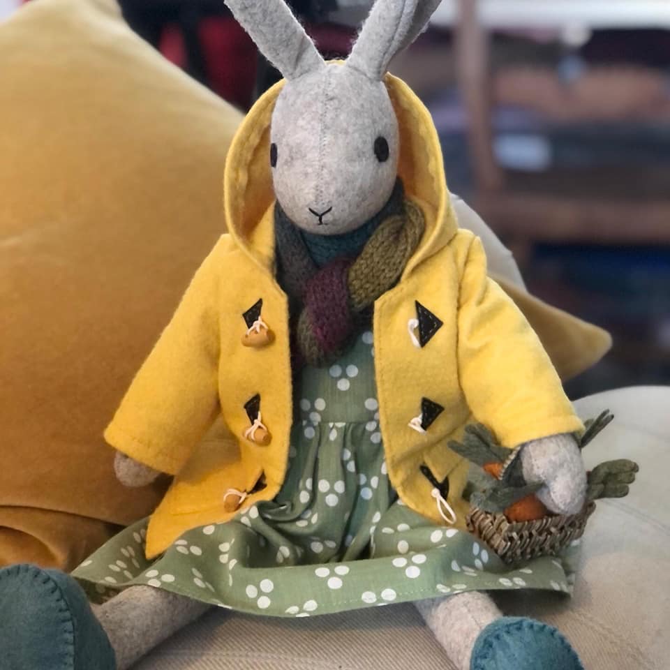 A handmade fabric bunny wearing a dress and yellow coat