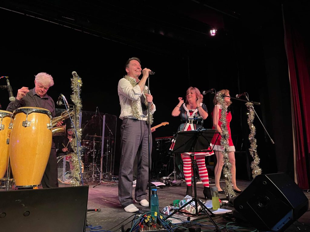 A band on stage wearing tinsel and festive decorations