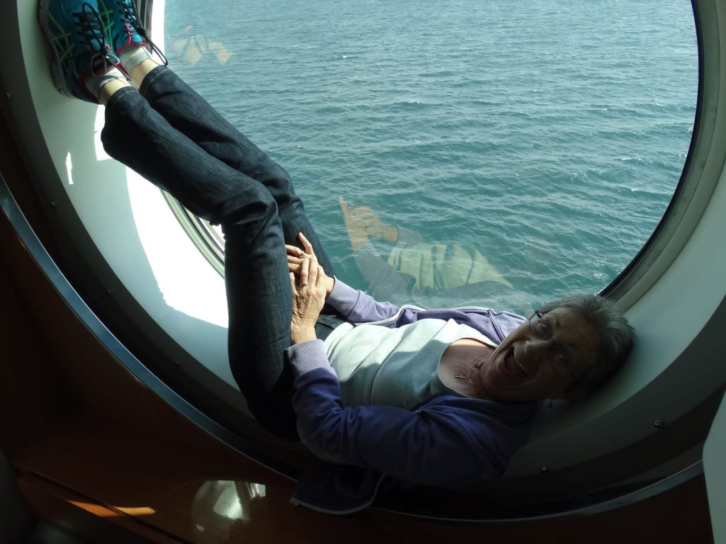 A woman lying in a porthole making a face at the camera