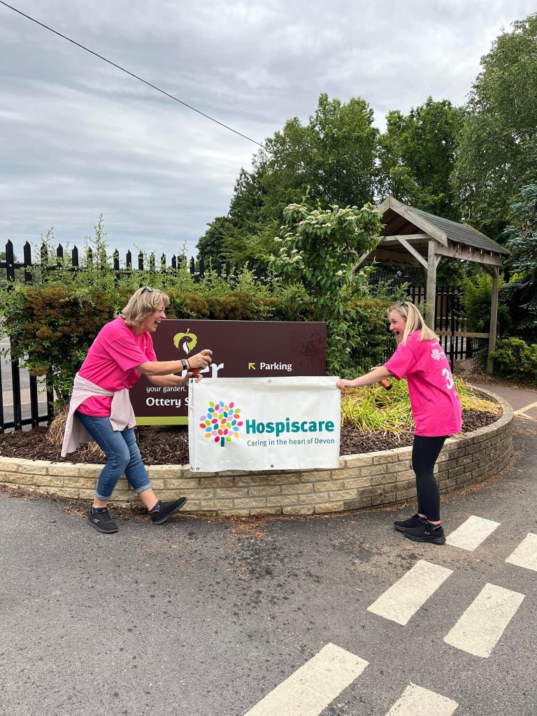 Two women in pink t-shirts holding a Hospiscare banner