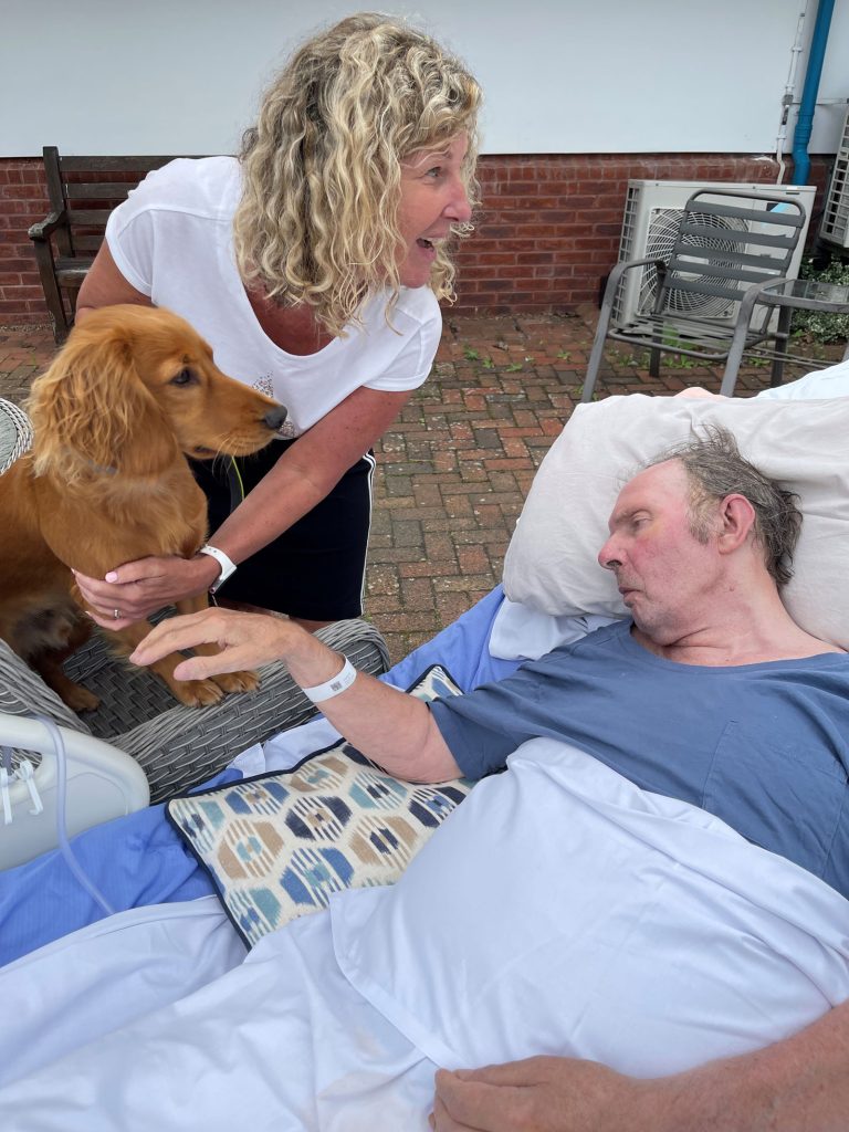 A woman and a dog with a man in a hospice bed outside
