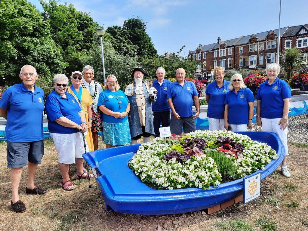 A group of people stood around a boat filled with flowers