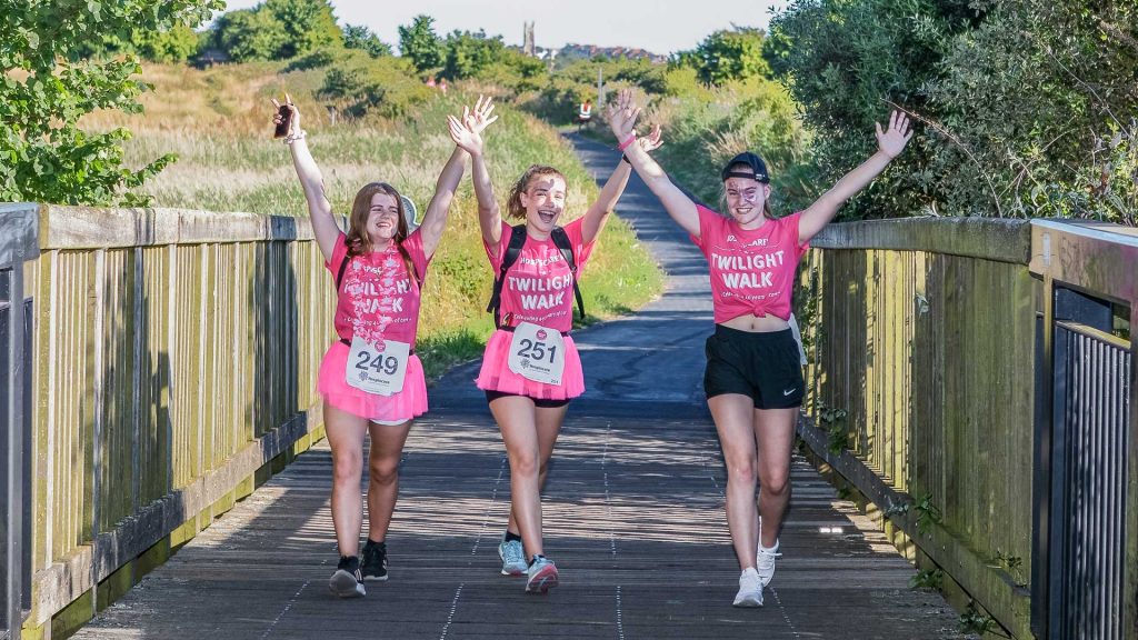 Three girls dressed in pink with their hands raised