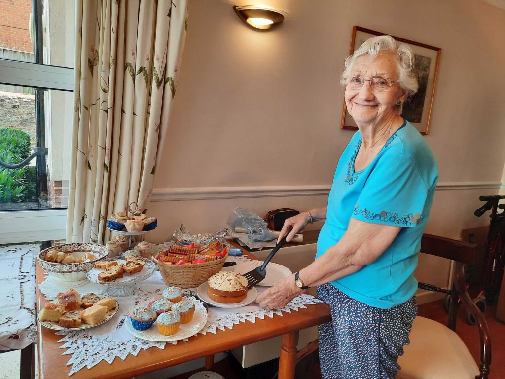 An elderly woman standing in front of a table full of cakes