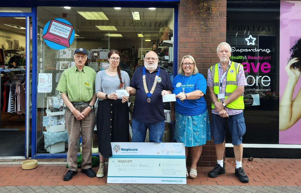 A group of people with a big cheque outside a charity shop