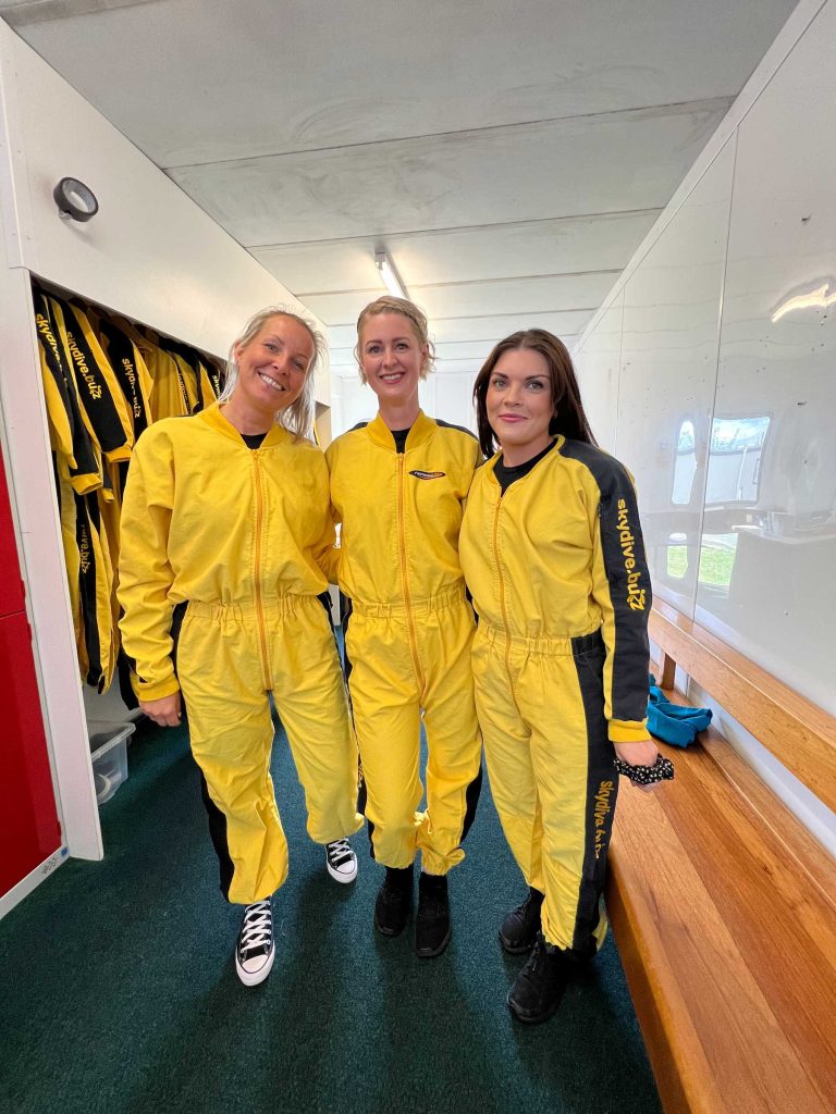 Three young women wearing yellow skydive jumpsuits