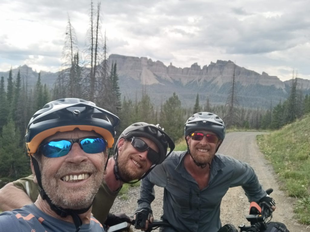 A selfie of three men wearing cycle helmets and sunglasses
