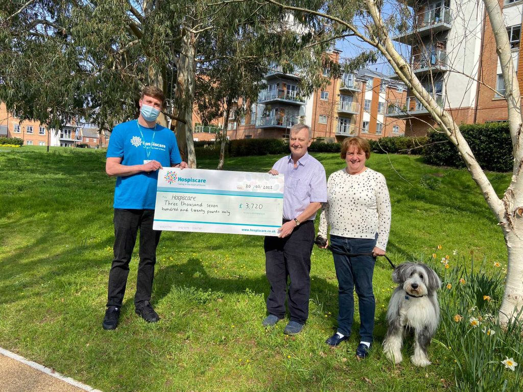A young man holding a big cheque with a couple and a dog outside