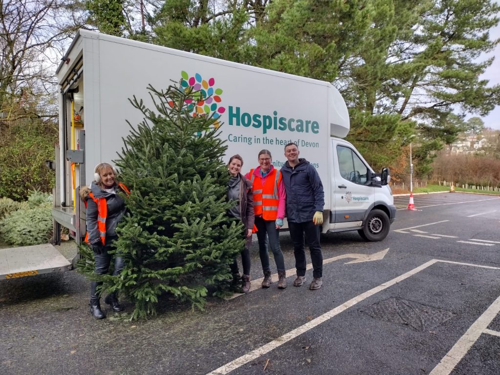 Four people with a real Christmas tree in front of a Hospiscare van