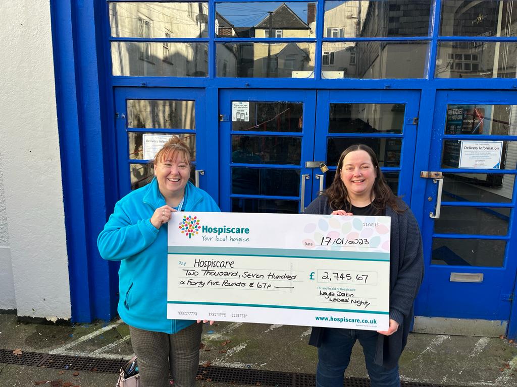 Two women holding a big cheque for Hospiscare outside a blue building