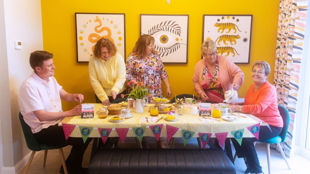 A group of people sat around a table sharing tea and cake